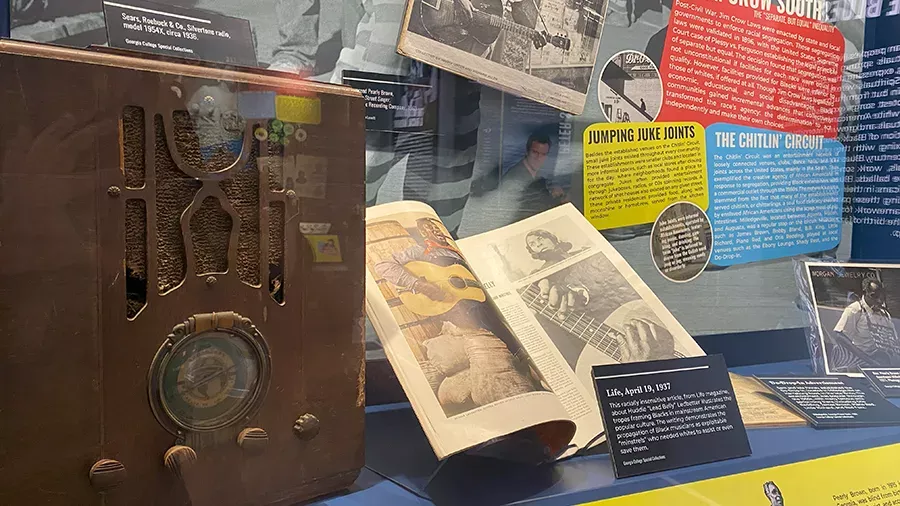 A museum exhibit showcasing an old radio, vintage magazines, and various informational panels. The heritage-focused display includes images and text about historical music culture, notably the "Jumping Juke Joints" and "The Chitlin' Circuit," with detailed descriptions of important dates and events.